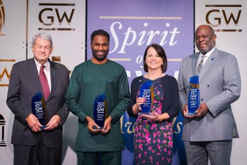 Four people, holding awards, posing in front of GW banners.
