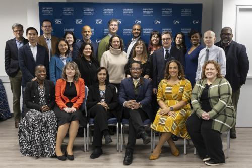 Faculty and staff from GW pose with Provost Christopher Bracey in front of a blue banner